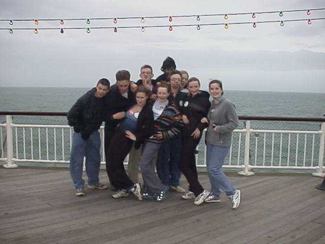 A group of young people posing comically on a British pier, in typical grey weather.