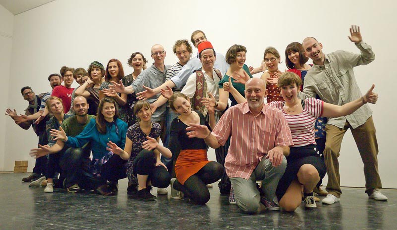 A group of people of all ages, smiling and waving at the camera, taken at a birthday tea dance.
